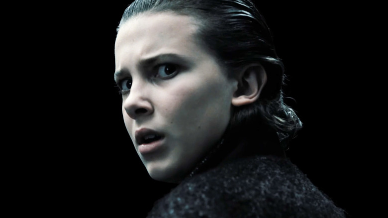 Millie Bobby Brown as Eleven looks back over her shoulder against a black background in Stranger Things