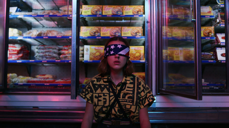 Millie Bobby Brown as Eleven sits blindfolded with a nosebleed in front of freezers filled with Eggo waffles in Stranger Things