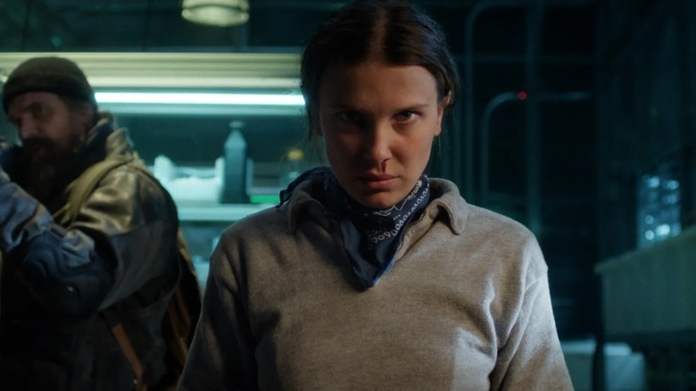 Eleven's nose bleeding, with Hopper off to the side holding an assault rifle, in Stranger Things