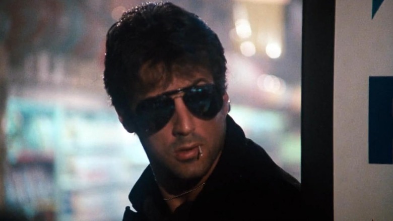 Marion Cobretti, dressing sunglasses, looks over the left shoulder in the cobra