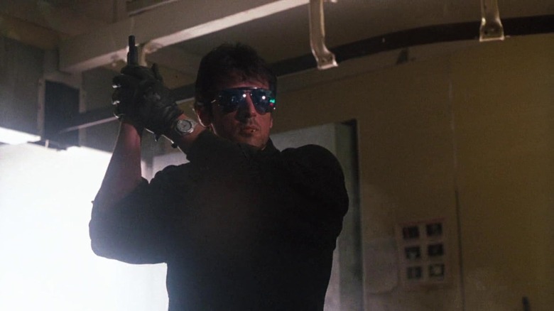 Marion Cobretti, putting on sunglasses, holding a gun upright in the cobra