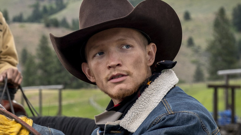 Jefferson White as Jimmy Hurdstrom wearing a cowboy hat and denim jacket saddling a horse on a ranch in Yellowstone