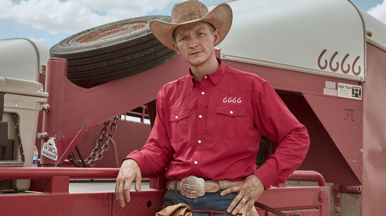 Jefferson White as Jimmy Hurdstrom wearing a cowboy hat and red shirt in front of a trailer in Yellowstone