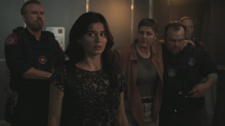 Ruby Cruz as Lily Dale with a concerned expression on her face standing next to Tyler Labine as Fred Stanislaus and several other characters in For All Mankind