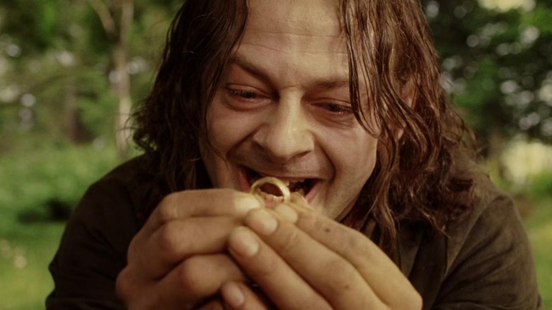 Andy Serkis as Sméagol holding up a gold ring and smiling in a woody area in The Lord of the Rings: The Return of the King