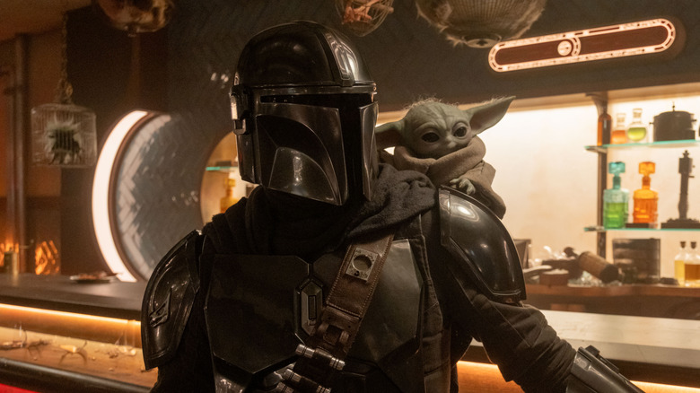 Mando standing at a bar with Grogu on his back in The Mandalorian and Grogu
