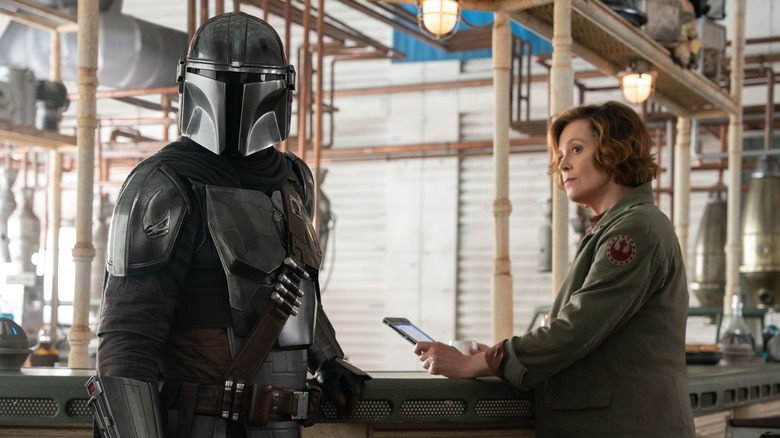 Pedro Pascal as Mando and Sigourney Weaver as Colonel Ward standing at a bar in The Mandalorian and Grogu