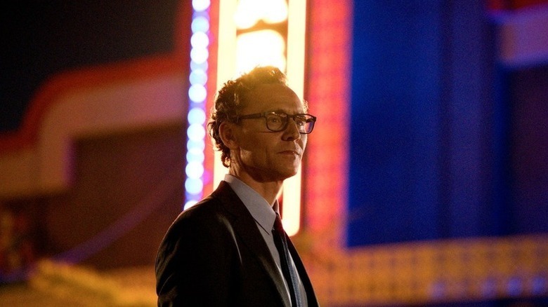 Tom Hiddleston as Charles "Chuck" Krantz standing in front of a neon sign in "The Life of Chuck"