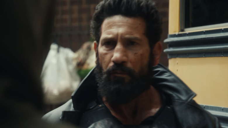 Jon Bernthal as Frank Castle walking past a school bus wearing his Punisher outfit in The Punisher: One Last Kill