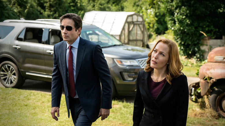 Molder, putting on the solar glasses, passes next to the rock in front of the parked machine on X-Files