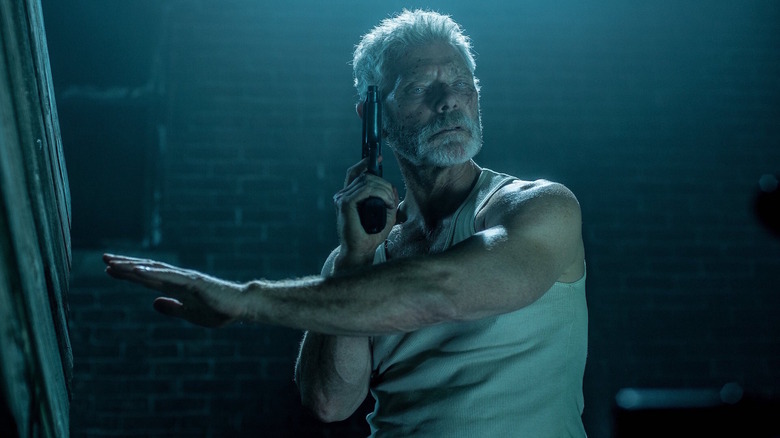Norman Nordstrom (Stephen Lang), also known as The Blind Man, holds a gun toward his temple and his hand out toward the wall in Don't Breathe 2 (2021)