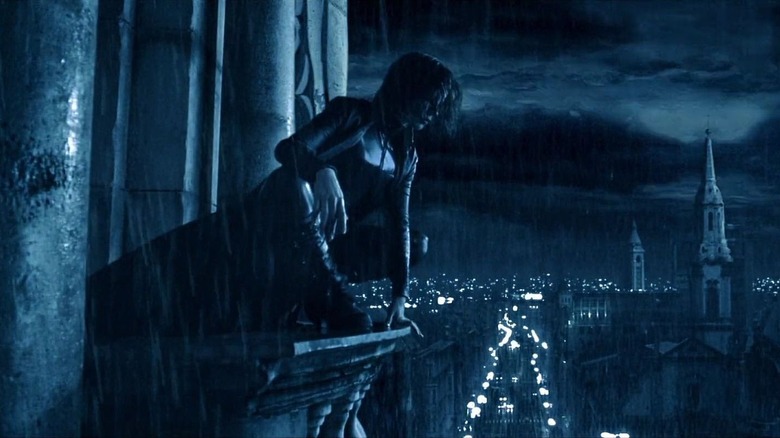 Selene (Kate Beckinsale) kneeling on a building pillar and staring out over a view of the city in Underworld (2003)