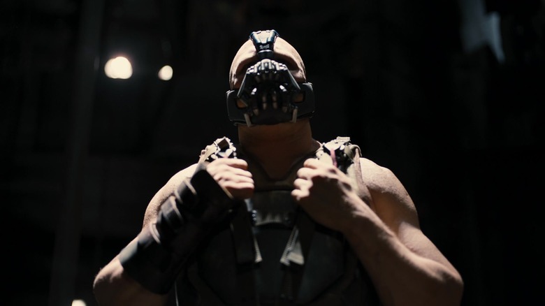 Tom Hardy's Bane rests his hands on his vest straps in The Dark Knight Rises