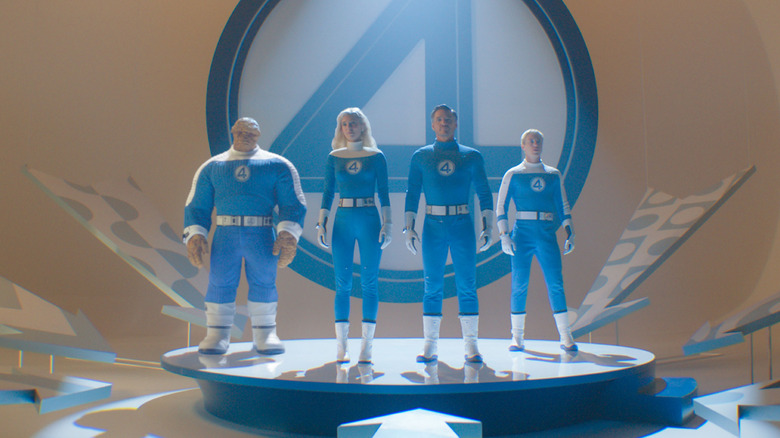 The Fantastic Four standing on stage in front of their 4 logo in matching blue spandex suits in The Fantastic Four: First Steps
