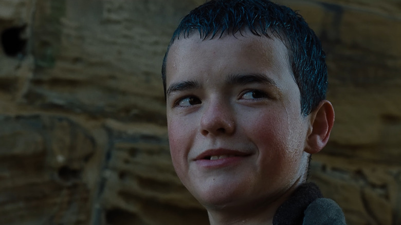 Owen Cooper as young Heathcliff soaked in the rain with a grin on his face in Wuthering Heights