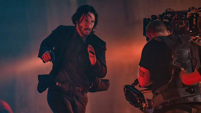 Keanu Reeves running toward a camera in a behind the scenes shot from a John Wick movie