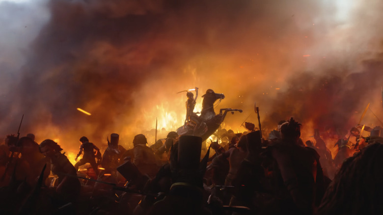 A figure raises a sword on horseback amid a fiery battleground in Wildwood