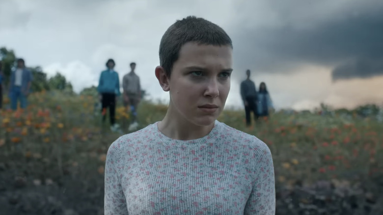 Milly Bobby Brown as Eleven stands on a hill looking out into the distance in Stranger Things