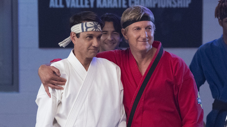 William Zabka as Johnny Lawrence with arm over Ralph Macchio as Daniel LaRusso's shoulder in Cobra Kai