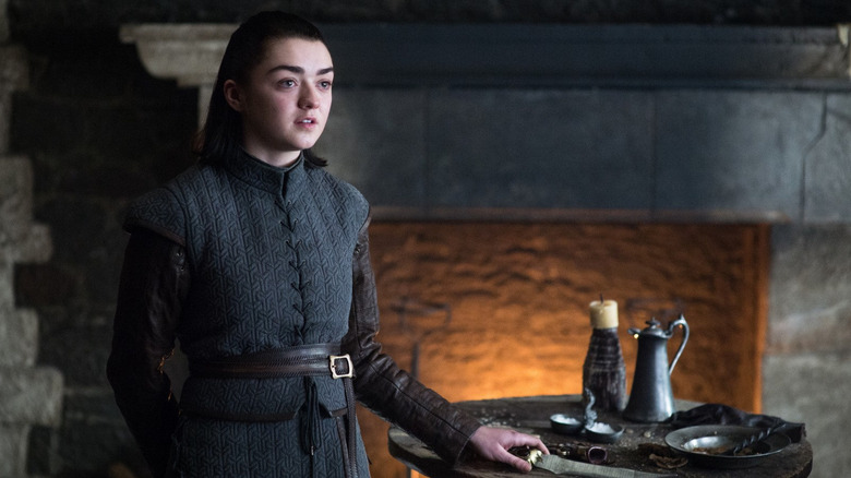 Arya Stark (Maisie Williams) stands by a table and a fireplace in Game of Thrones