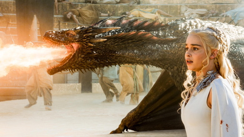 Daenerys Targaryen (Emilia Clarke) stands next to a dragon breathing fire in Game of Thrones