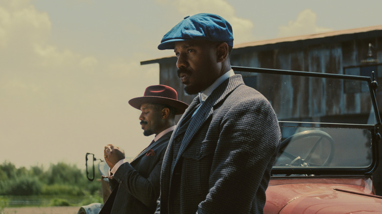 Michael B. Jordan as twins Smoke and Stack leaning against a car in Sinners