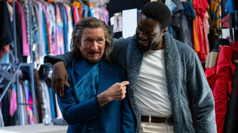 Yahya Abdul-Mateen II as Simon Williams embracing Sir Ben Kingsley as Trevor Slattery in front of racks of colorful costumes in Wonder Man