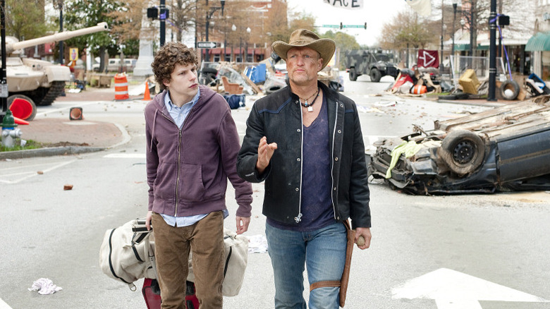 Columbus (Jesse Eisenberg) and Talhaasi (Woody Harluson) stand together in the destroyed streets in 