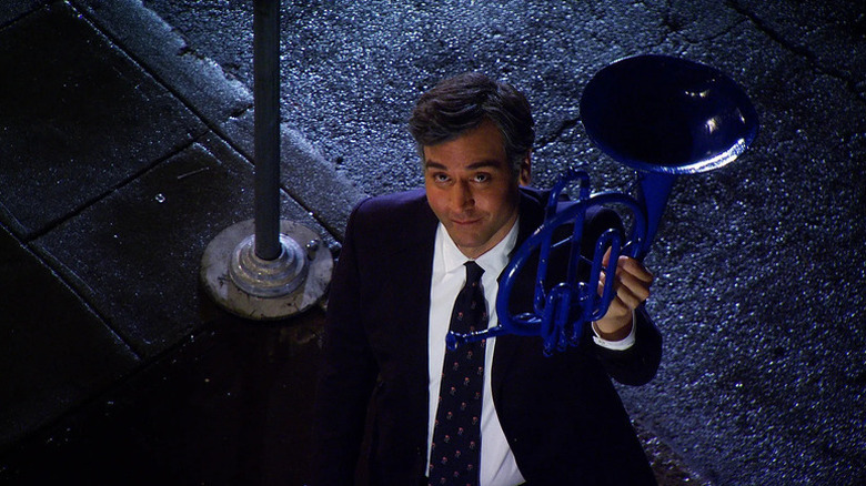 An older Ted Mosby (Josh Radnor) holds up a blue French horn while looking up from a sidewalk on How I Met Your Mother