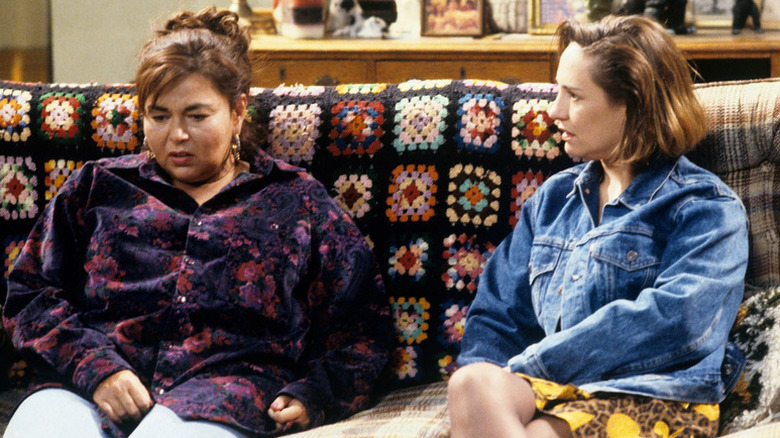 Roseanne Conner (Roseanne Barr) sits in shock on the couch next to Jackie Harris (Laurie Metcalf) in Roseanne