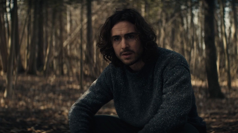 man with long dark hair sitting in the woods