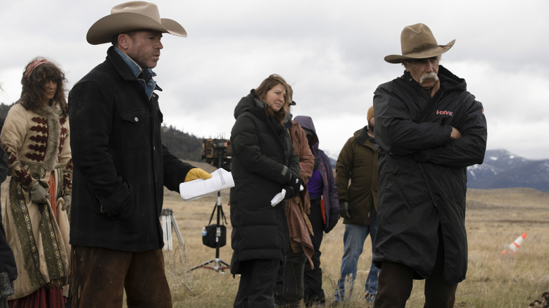 Sam Elliott as Shea standing in a coat next to Taylor Sheridan holding a script in a behind-the-scenes still from 1883