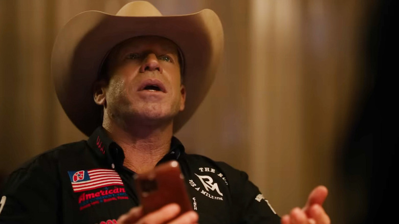 Taylor Sheridan's Travis Wheatley looks up as he sits at a table holding his phone in Yellowstone