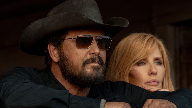 Cole Hauser's Rip Wheeler looks off into the distance wearing shades next to Kelly Reilly's Beth Dutton in Dutton Ranch