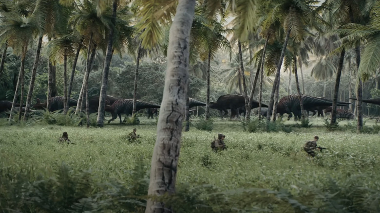 Soldiers walk through long grass while chasing dinosaurs in the background in the primitive war