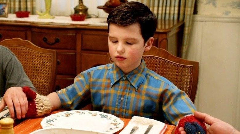 Iain Armitage's Sheldon sitting at the dinner table with his mittens on in Young Sheldon