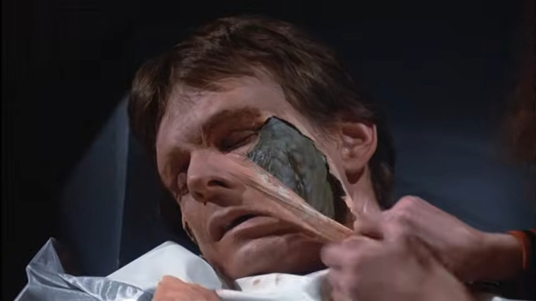 Een man die zijn menselijke huid afpelt om een reptielengezicht eronder te onthullen in V: The Final Battle