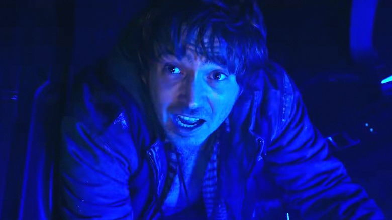 Bryan crawls in the interior of a cop car, illuminated by blue light, in Resident Evil