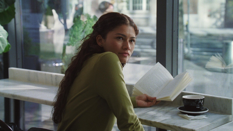 Zendaya as Emma sitting at a coffee shop reading her book in The Drama