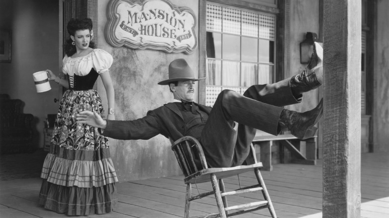 Henry Fonda as Wyatt Earp leans back in a chair on a porch while Linda Darnell as Chihuahua looks on in My Darling Clementine